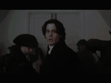a man in a black coat and white shirt is standing in front of a group of people .