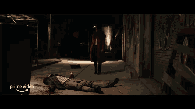 a woman in a red coat stands next to a man laying on the ground in a dark alleyway with the words prime video visible