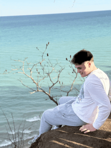 a young man sits on a rock near the ocean