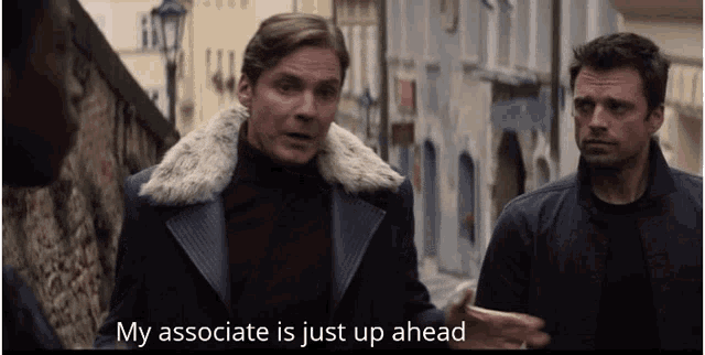 a man in a fur coat says " my associate is just up ahead " while standing next to another man