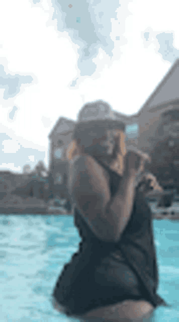 a woman is kneeling in a swimming pool wearing a hat and sunglasses .