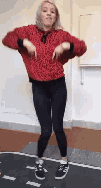 a woman in a red hoodie and black leggings is dancing on a mat .