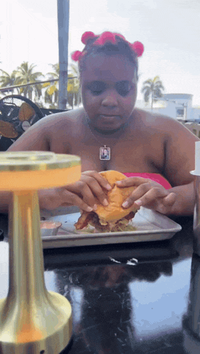 a woman sitting at a table eating a sandwich with a picture of a man on her necklace