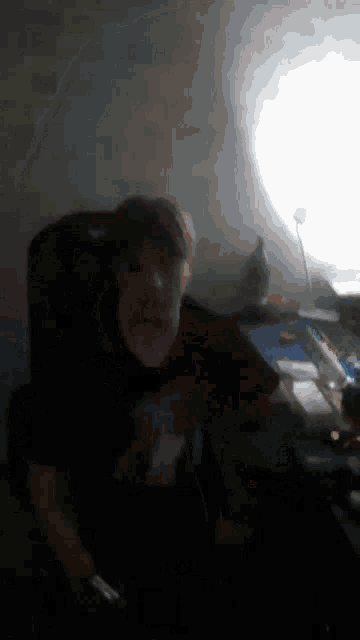 a man in a black shirt is sitting in a dark room holding a remote control
