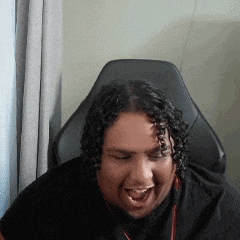 a man with curly hair is sitting in a chair with his mouth open and laughing .