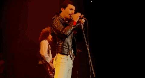 a man is singing into a microphone on a stage while another man stands behind him .