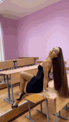 a woman in a black dress sits on a desk in a classroom