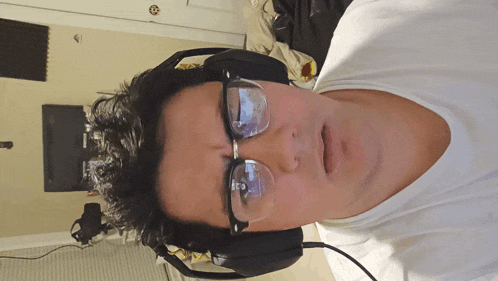 a man wearing glasses and headphones looks at the camera with a surprised look on his face