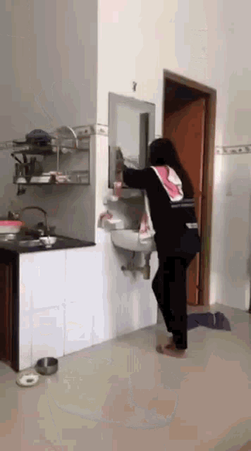 a woman is standing in front of a sink in a kitchen looking at herself in the mirror .