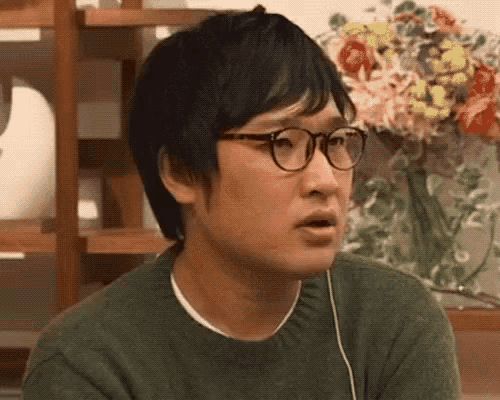 a man wearing glasses and a green sweater is making a funny face .