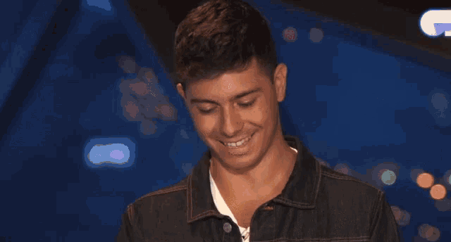 a young man in a denim jacket is smiling and looking down