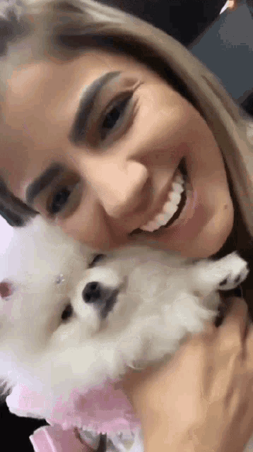 a woman is smiling while holding a small white dog in her arms .