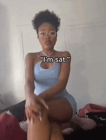 a woman in a blue dress is sitting on a bed with her legs crossed and says " i 'm sat " .