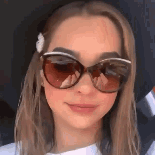 a woman wearing sunglasses and a hat is smiling .