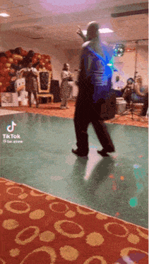 a man is dancing on a green dance floor in a room with balloons in the background .