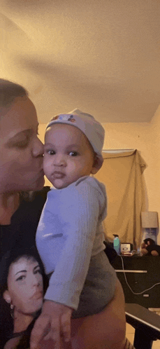 a woman is holding a baby in her arms and kissing him on the cheek