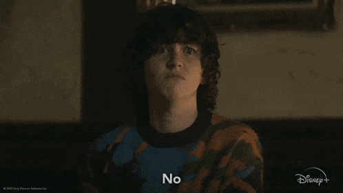 a young man with curly hair is wearing a camouflage sweater and saying no .