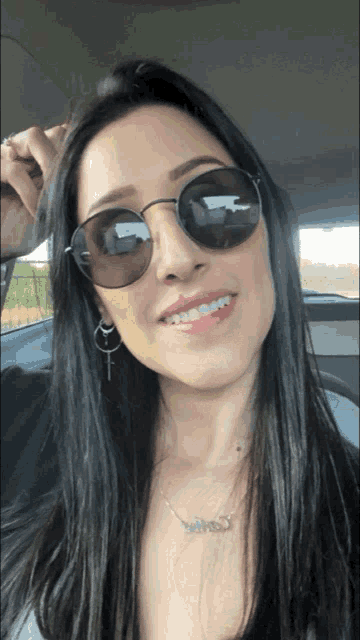 a woman wearing round sunglasses and a necklace with the word jesus on it