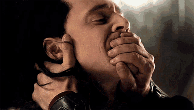 a close up of a man covering his mouth with his hands .