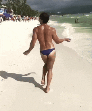 a shirtless man in blue swim trunks is walking on a beach