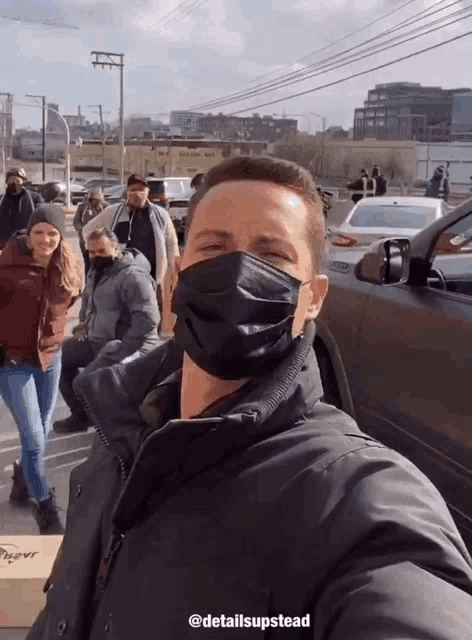 a man wearing a black face mask is taking a selfie with a group of people in a parking lot