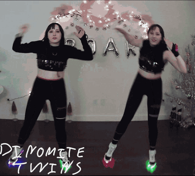 two women are dancing in front of a sign that says " dynamite twins " on it