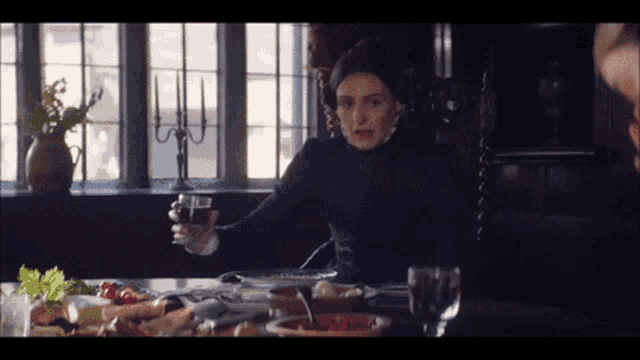 a woman is holding a glass of wine while sitting at a table with food .