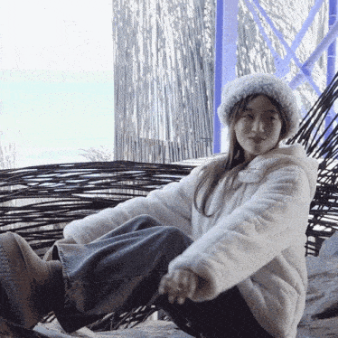 a woman wearing a white hat and a white jacket sits on a rock