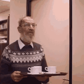 a man in a sweater holds a tray of cups and saucers