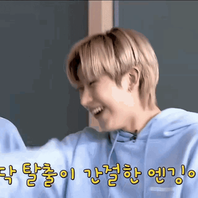 a young man wearing a blue hoodie is laughing in korean writing