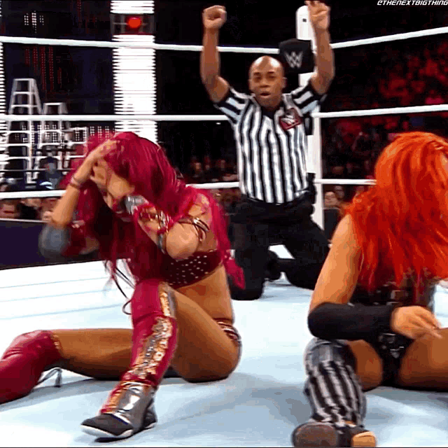 a woman with red hair is kneeling down in a wrestling ring with a referee in the background