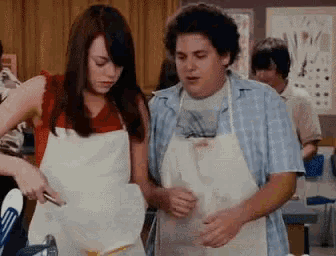 a man and a woman are standing next to each other in an apron .