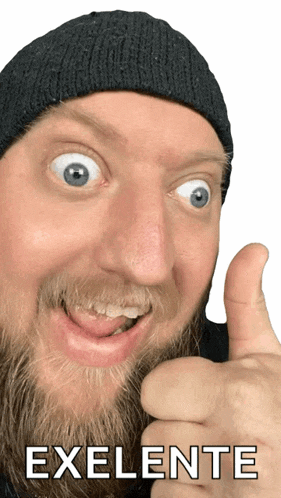 a man with a beard wearing a black hat gives a thumbs up with the word exlente behind him
