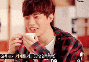 a young man in a plaid shirt is drinking from a cup .