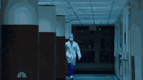 a man in a lab coat is walking down a hallway with an exit sign on the wall