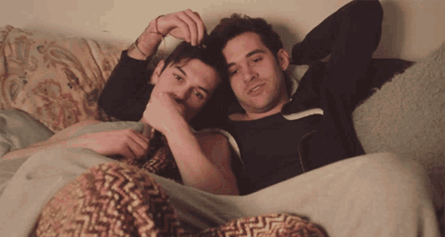 two men are laying on a couch and one of them is touching the other 's head