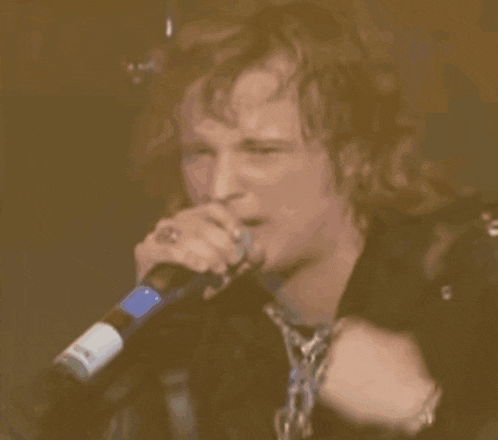 a close up of a man singing into a microphone with a bottle of beer in front of him