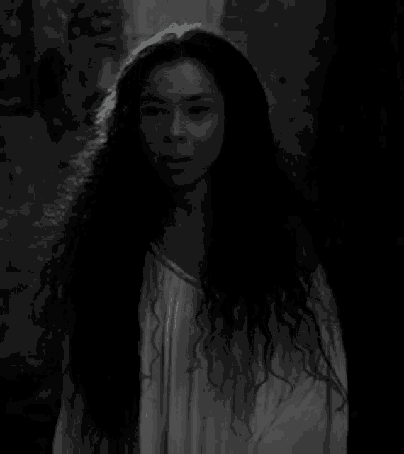 a black and white photo of a woman with long curly hair in a white dress .