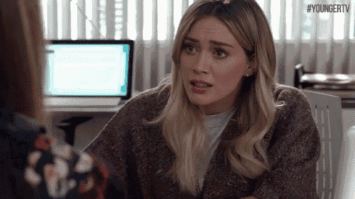 a woman in a sweater is talking to another woman in front of a laptop .