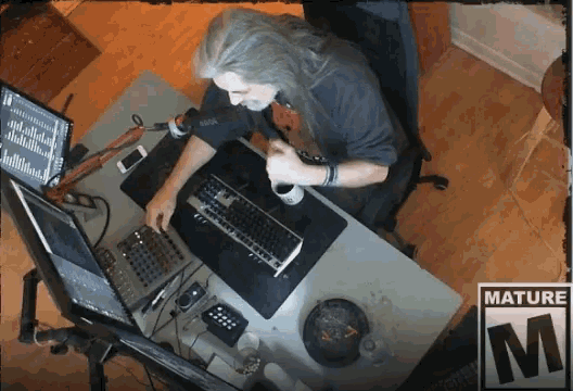 a man sits at a desk in front of a computer with a mature m sticker