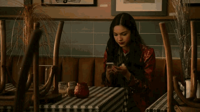 a woman sits at a table with a checkered tablecloth looking at her phone