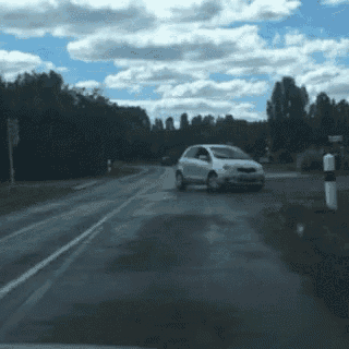 a white car is driving down a road in the countryside