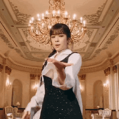 a woman in a black dress is dancing in a room with a chandelier in the background .