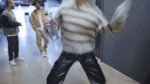a man in a striped sweater and leather pants is dancing in a hallway while two other men watch .