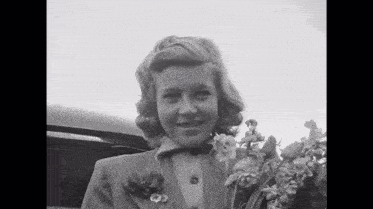 a woman in a suit is holding a bouquet of flowers and smiling .