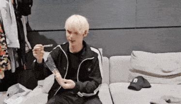 a man in a black jacket is sitting on a couch eating something with a spoon