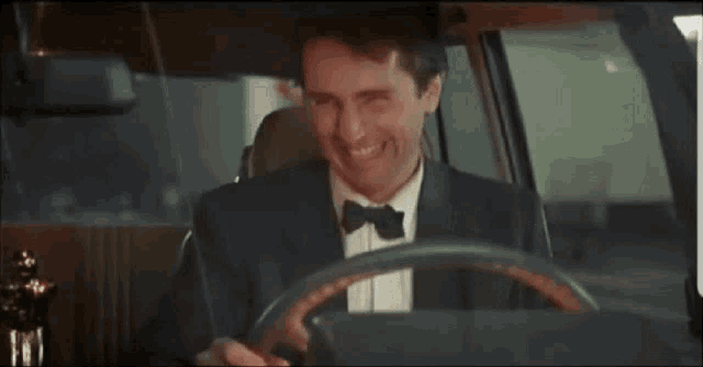 a man in a suit and bow tie is driving a car and smiling