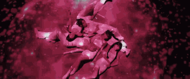 a group of people are dancing in a dark room with a pink background .
