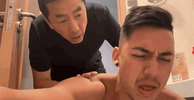 a man in a black shirt is giving another man a massage in a bathroom