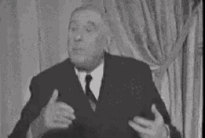 a man in a suit and tie is standing in front of a curtain and making a funny face .